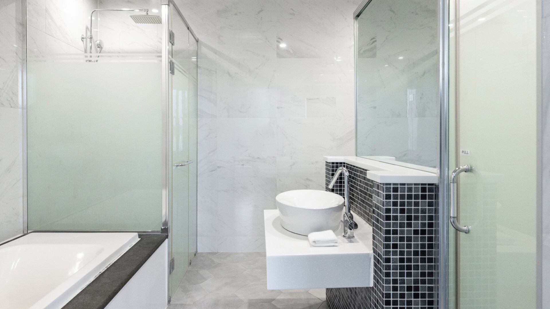 Une salle de bain moderne avec une douche à parois de verre, une baignoire blanche et un lavabo avec un pare-éclaboussures en carreaux noirs.