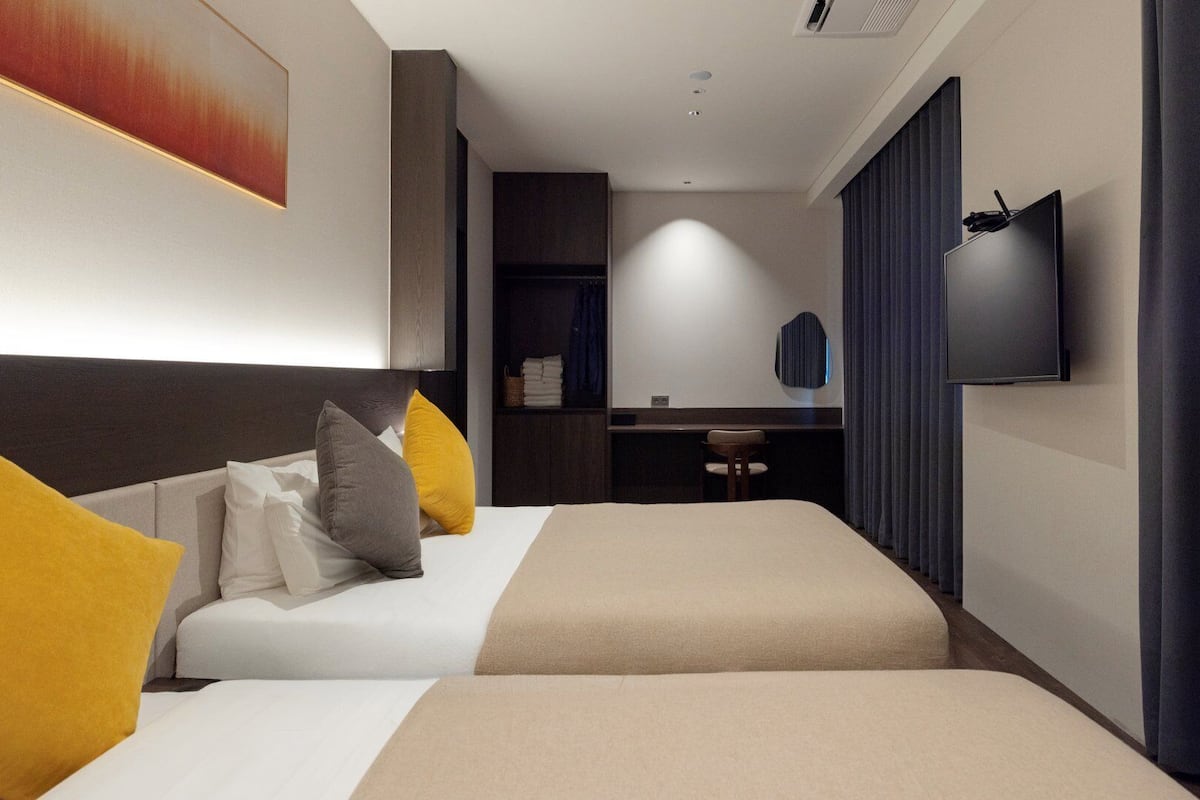 A hotel room with two beds, a desk, a TV, and a wardrobe.