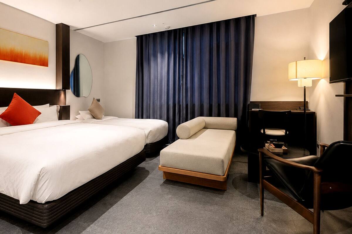 A hotel room with a large bed, two smaller beds, a sofa, a desk, and a TV.
