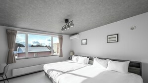 A modern bedroom with a large bed, a window with curtains, a radiator, and a ceiling light fixture. - HILLS NISEKO E (Niseko)