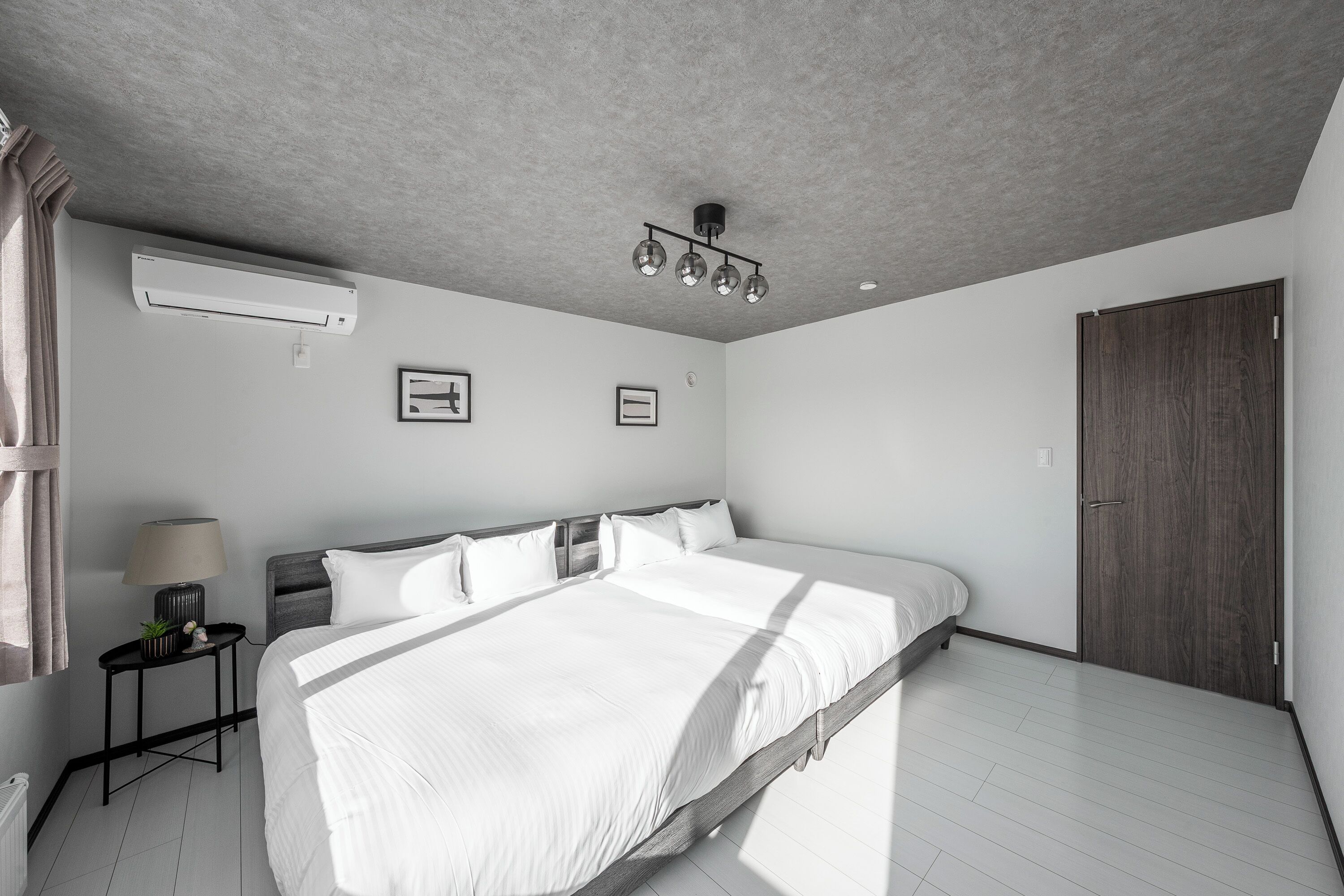 A modern bedroom with a large bed, a ceiling light fixture, and a wardrobe.