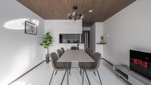 A modern living room with a dining table, grey chairs, a TV displaying 'NETFLIX', and a wooden ceiling. - HILLS NISEKO E (Niseko)