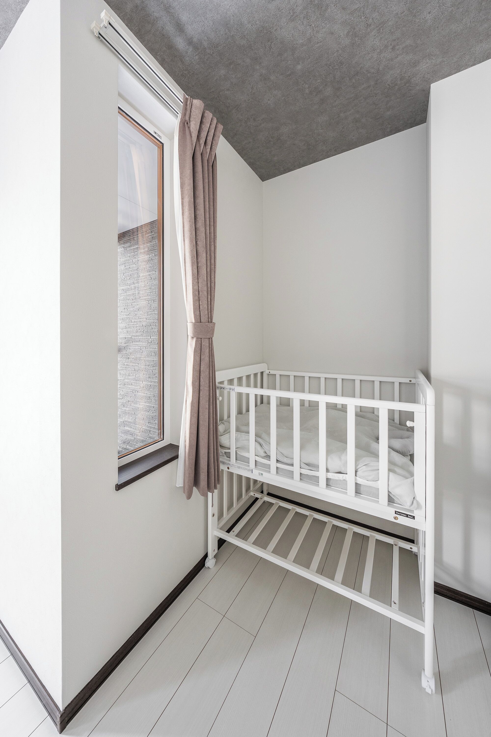 Una cuna blanca en una habitación con ventana y cortina.