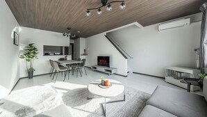 A modern living room with a sofa, coffee table, and a TV. There's a staircase, a dining area, and a kitchen in the background. - HILLS NISEKO E (Niseko)