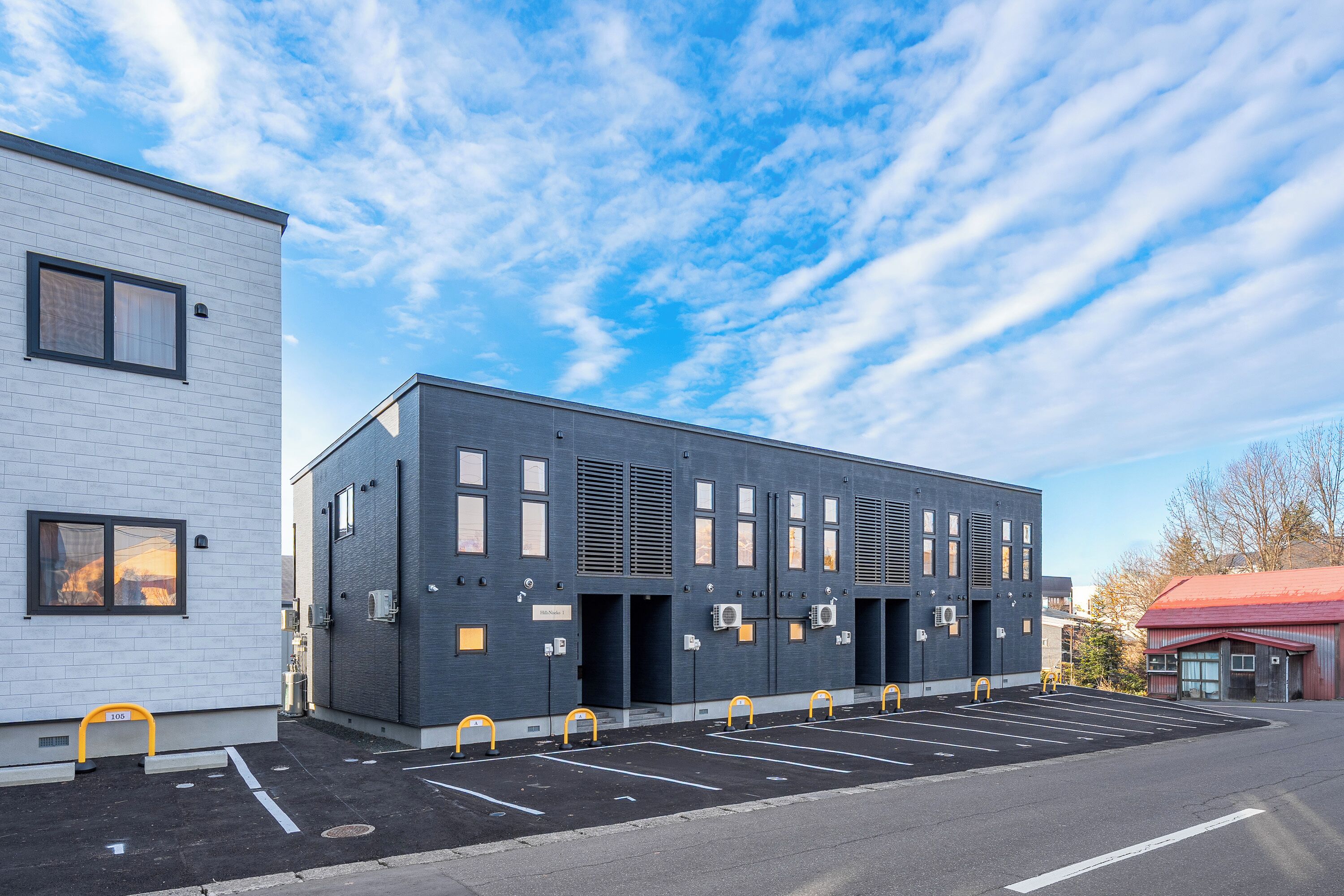 A modern building with a parking lot, featuring a row of parking spaces and a building entrance.
