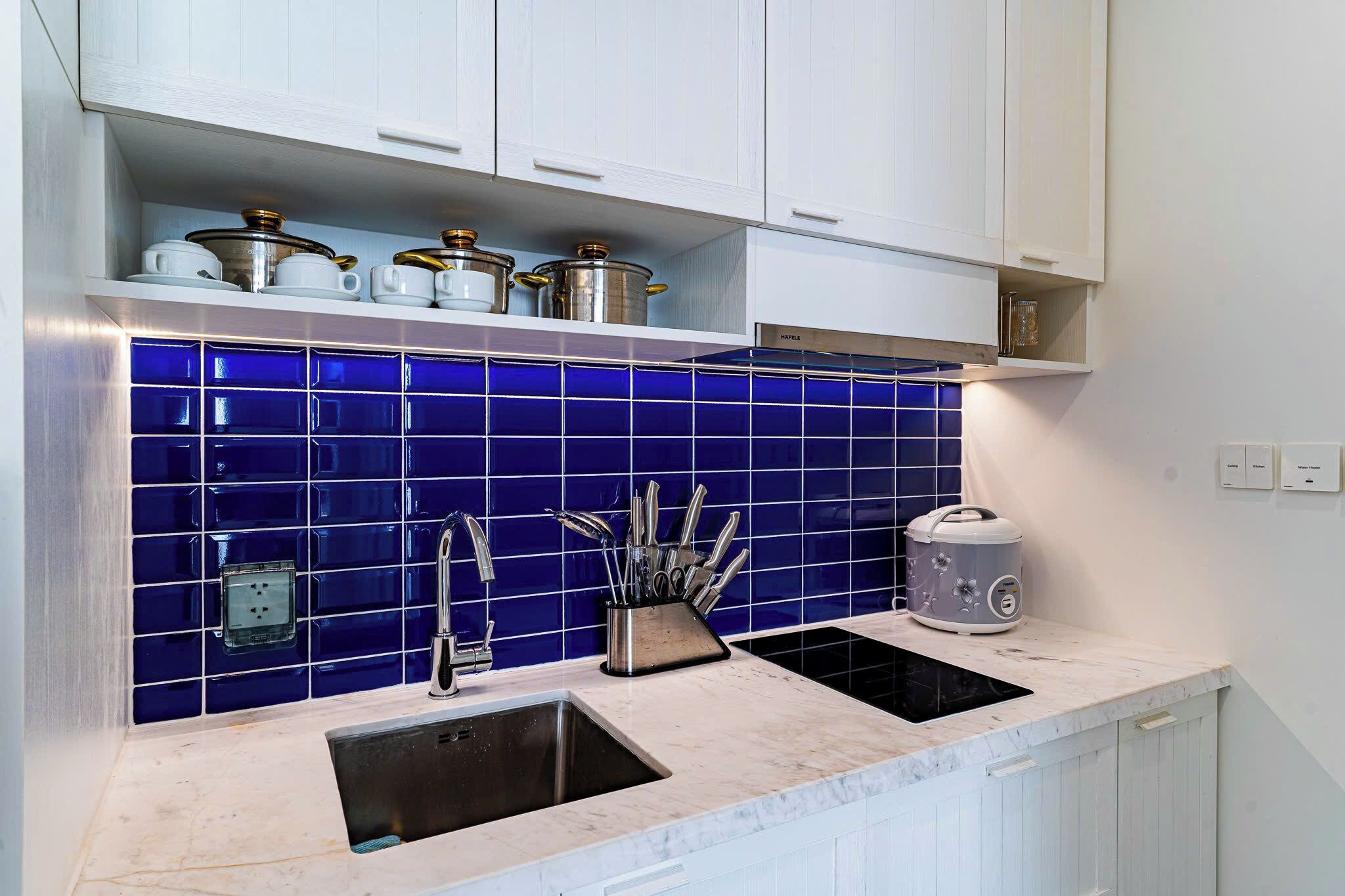 Een keuken met een blauwe betegelde achterwand, een gootsteen, een fornuis en witte kastjes.
