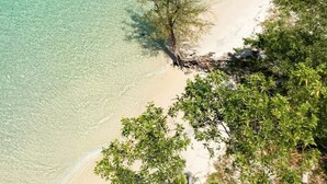 Una playa con agua turquesa cristalina, una orilla arenosa y abundante vegetación verde.
