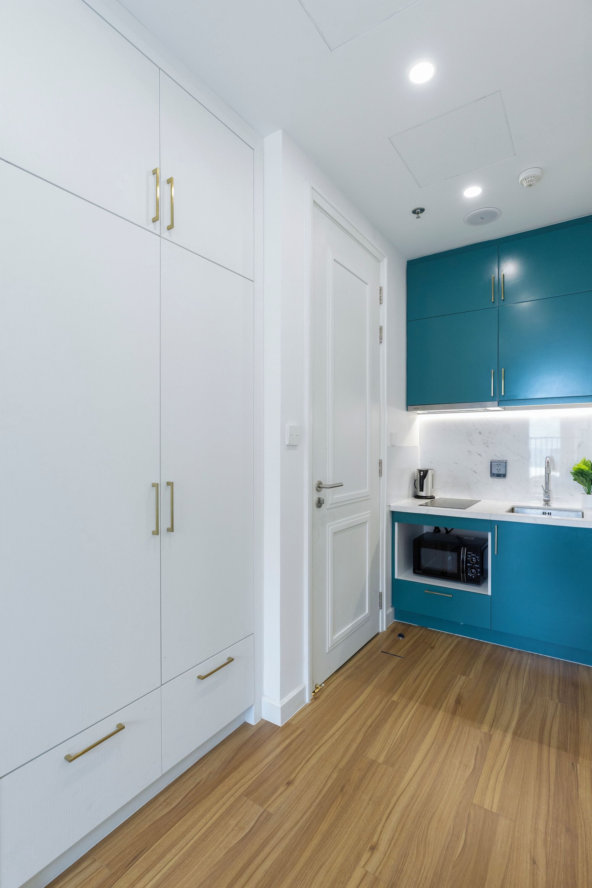 A modern kitchen with white cabinetry, teal accents, and a wooden floor.