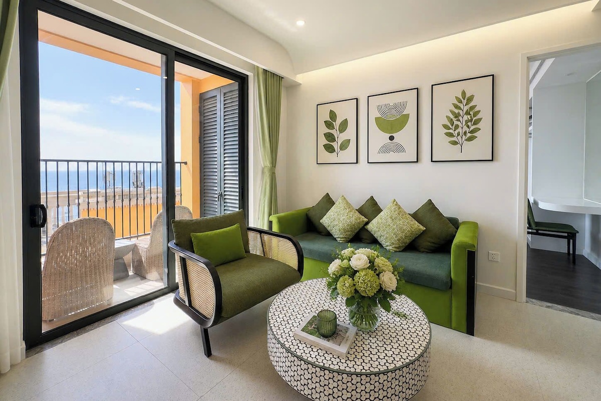 A modern living room with a balcony, a green sofa, a round coffee table, and framed artwork on the wall.