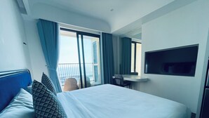 Habitación de hotel con una cama grande, un escritorio, un televisor y un balcón con cortinas.
