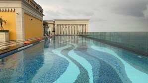 Una piscina con suelo de baldosas, una barrera de cristal y un edificio de arquitectura clásica al fondo.