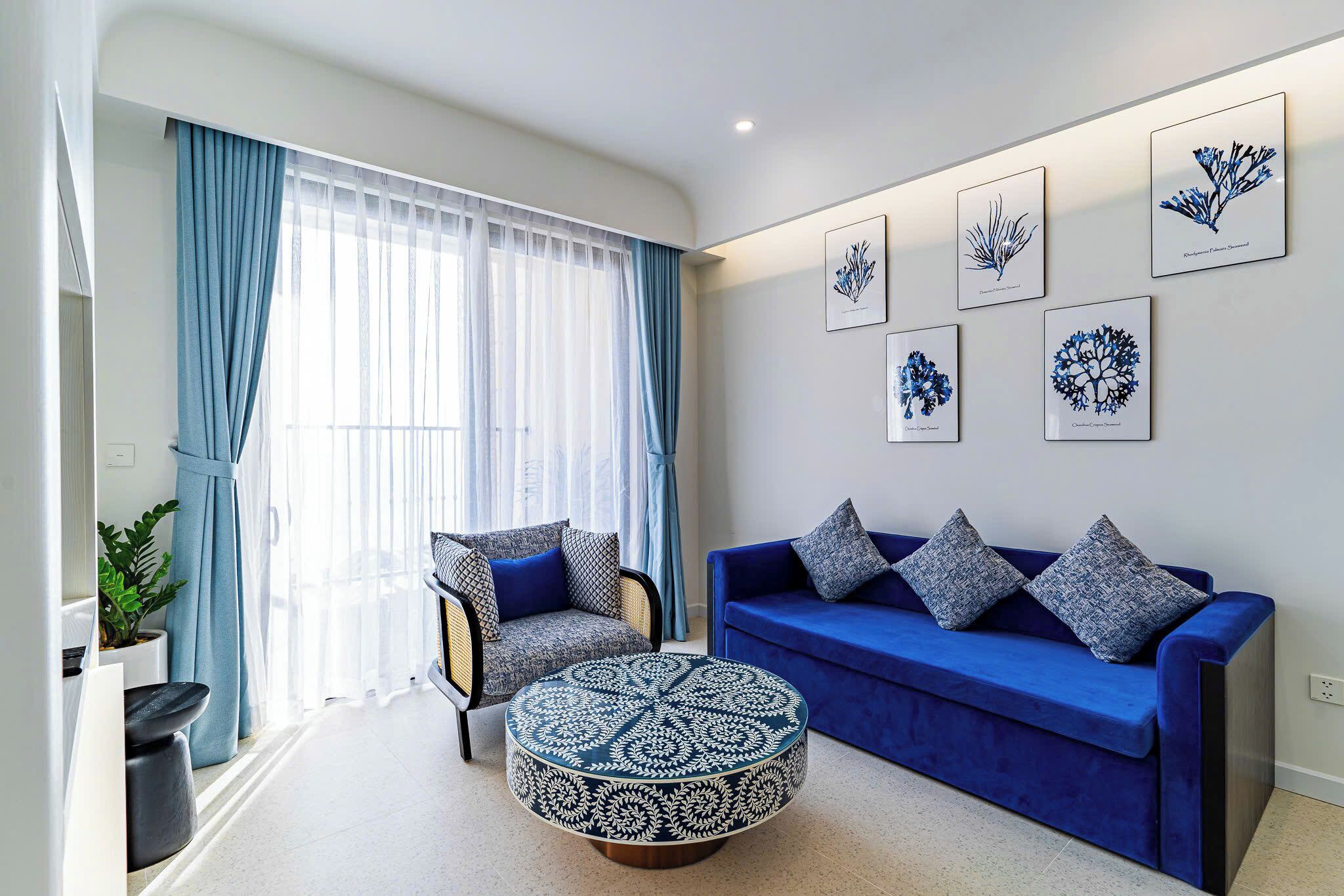 A living room with a blue sofa, two armchairs, a round coffee table, and a potted plant.