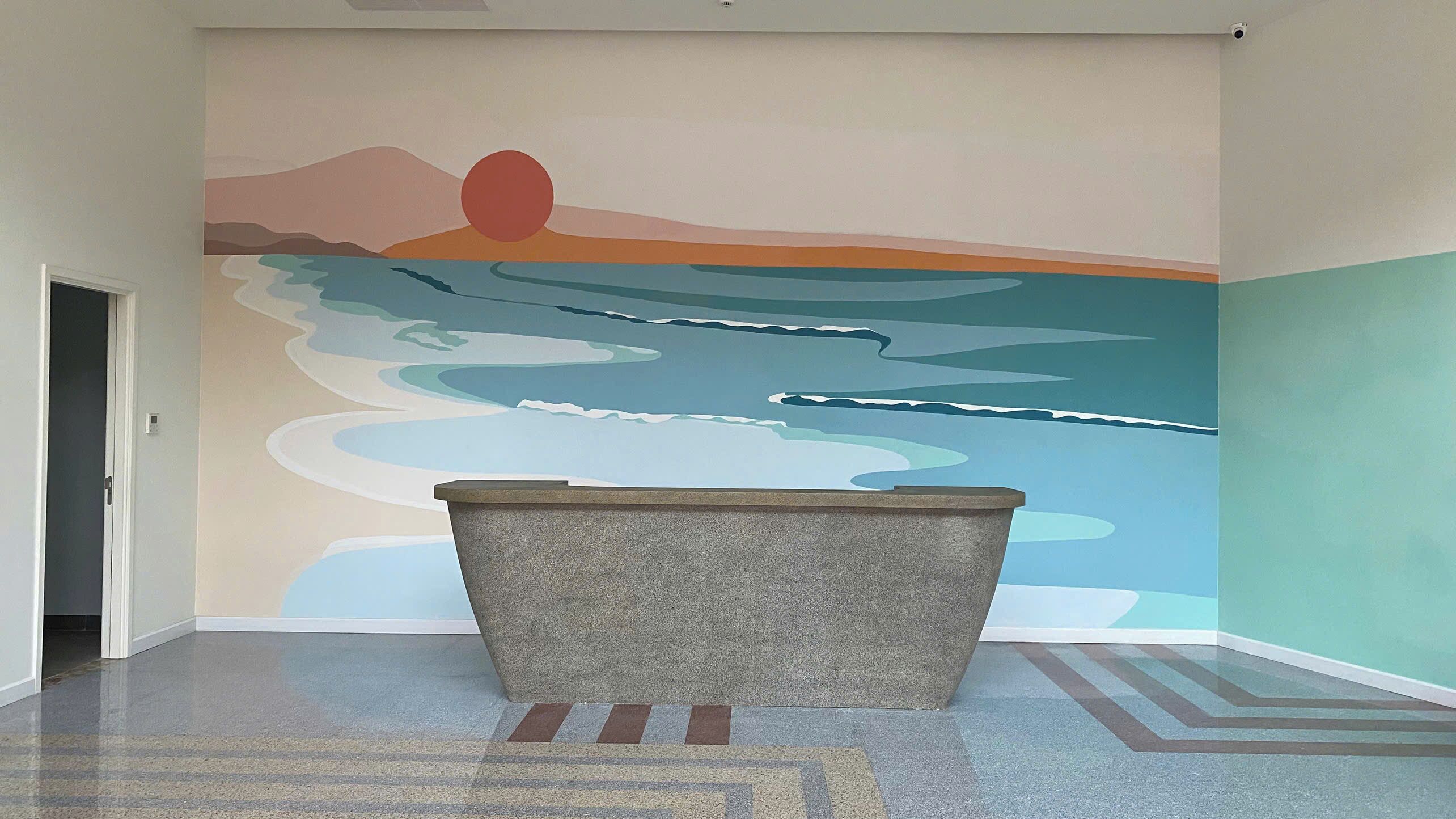 Una habitación con un mural de una puesta de sol sobre el océano, un banco de piedra y un piso con diseño.