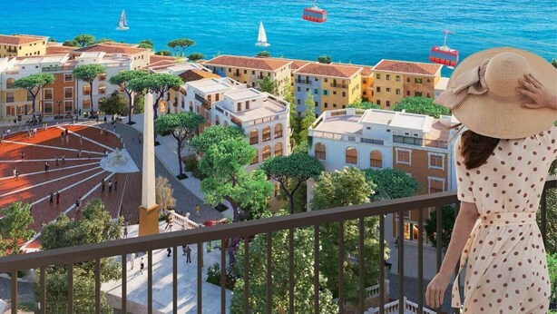 Un balcón con vistas a un pueblo costero, que incluye edificios, árboles y barcos en el agua.