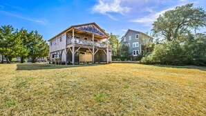 A two-story wooden building with a balcony, surrounded by a grassy field and trees. - Canalfront, Cozy 3BR with Amazing sound views! (Frisco)