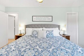A bedroom with a large bed, two bedside tables, and a framed sign on the wall.