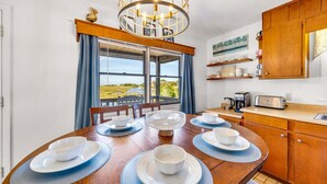 A dining area with a view of a natural landscape, a wooden dining table with plates and bowls, a chandelier, and a kitchen area with a toaster and coffee maker. - Canalfront, Cozy 3BR with Amazing sound views! (Frisco)