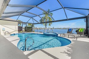 A swimming pool with a view of the water, surrounded by lounge chairs and a covered area. - Quiet & Private Retreat on Thunderbird Lake | Heated Pool, Gulf Access | Sleeps 6 (Cape Coral)