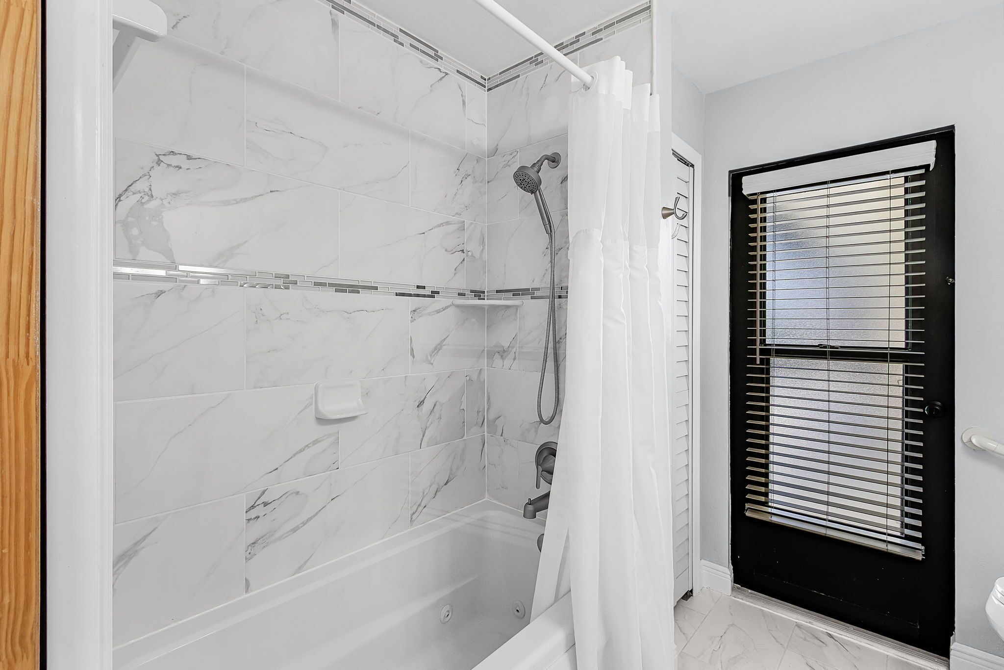 A bathroom with a shower, tiled walls, a bathtub, and a door with blinds.