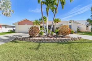 A residential property with a well-maintained lawn, stone border, and palm trees. - Quiet & Private Retreat on Thunderbird Lake | Heated Pool, Gulf Access | Sleeps 6 (Cape Coral)
