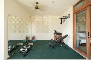 A gym with exercise equipment, a mirror, and a bed in a room with a sliding glass door. - Manu Made - 3-Bedroom, Bunk Room, Gym, Ice bath (Bali)