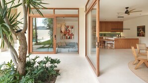 Ein modernes Interieur mit einer Glastür, die in einen Wohnbereich führt, einer Küche mit Holzschränken und einem Essbereich mit Tisch und Stühlen.