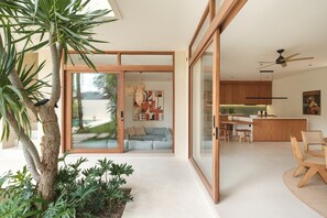 Ein modernes Interieur mit einer Glastür, die in einen Wohnbereich führt, einer Küche mit Holzschränken und einem Essbereich mit Tisch und Stühlen.