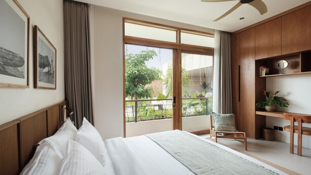Ein Hotelzimmer mit einem großen Bett, einem Holztisch, einem Stuhl und einem Balkon mit Blick auf Grünflächen.