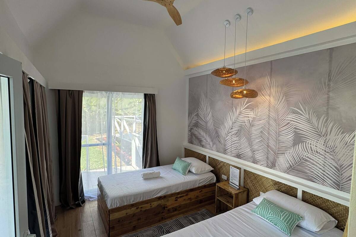 A bedroom with two beds, a ceiling fan, and a large window with curtains.