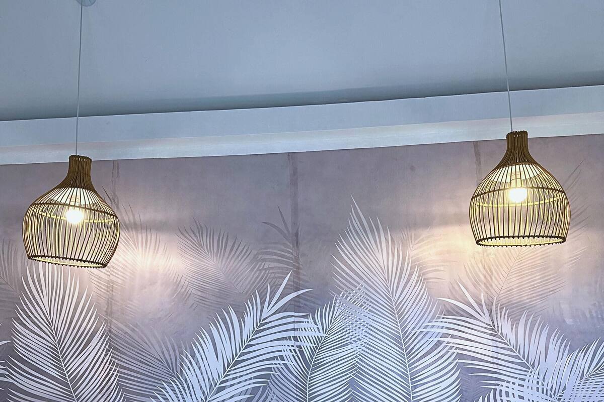 A room with two hanging wicker lamps, a white bed with a woven headboard, and a wall with a leaf pattern.