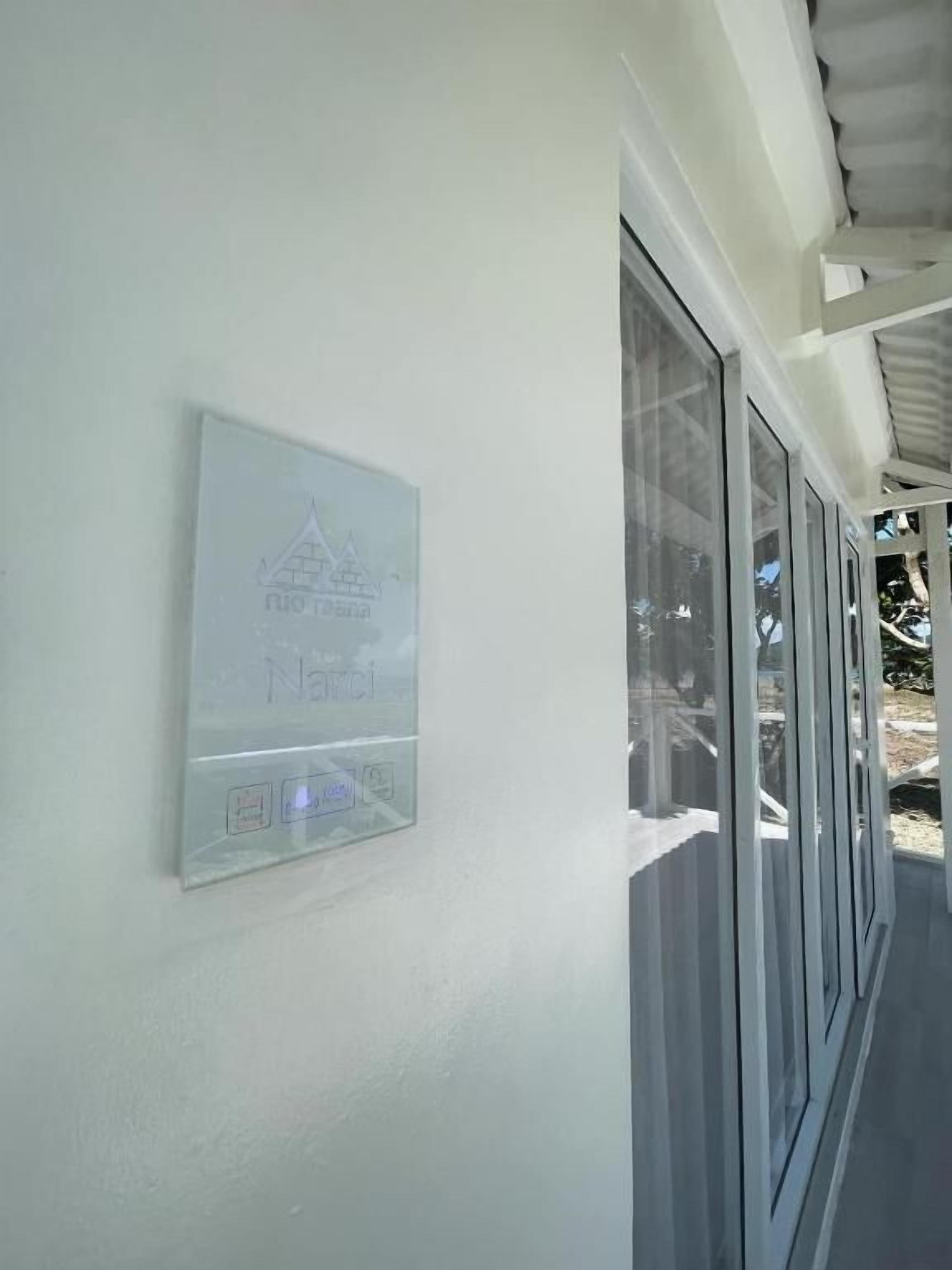 A wall-mounted sign with a logo and text, next to a window with a view of trees and a building.