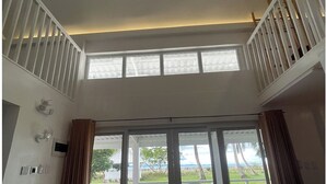 A spacious room with a ceiling fan, large sliding glass doors leading to an outdoor area with chairs and a view of the beach. - Riomana Villas Resort and Cafe (Cateel)