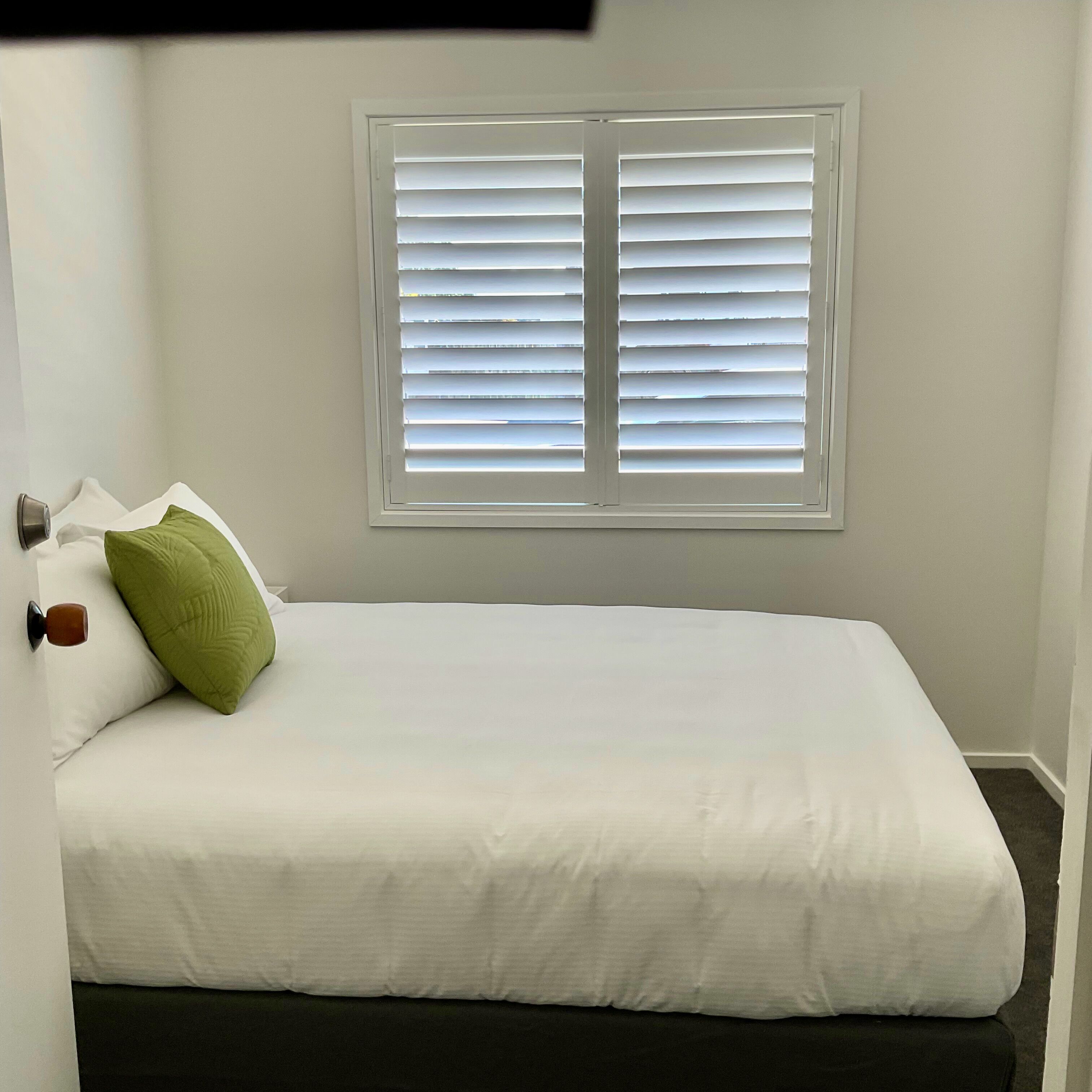 A single bed with white bedding, a green pillow, and a window with closed blinds.