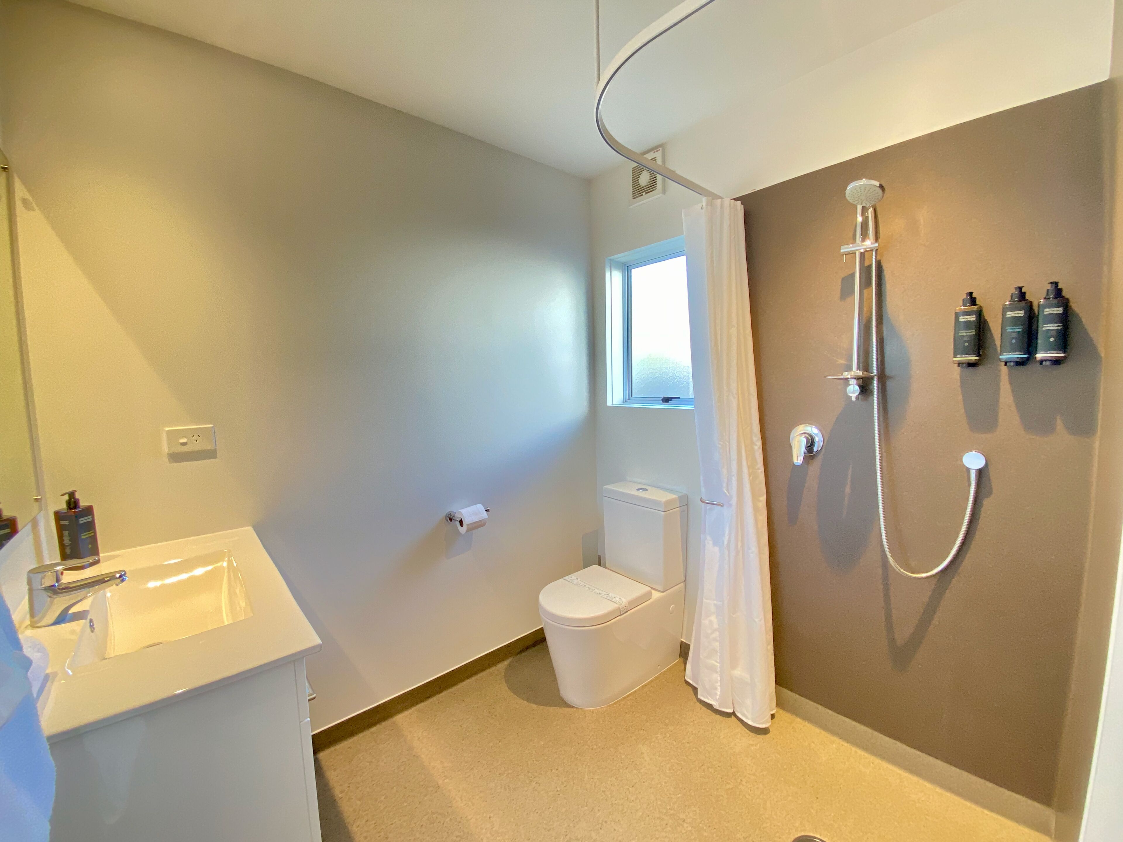 A bathroom with a toilet, sink, shower, and a window.