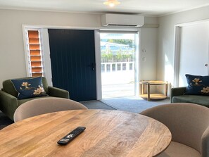 A room with a wooden table, two green armchairs with floral cushions, and a dark blue door. - Pioneer Motel (Collingwood)