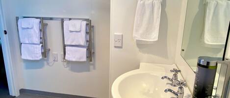 Ein Badezimmer mit einem weißen Waschbecken, zwei Wasserhähnen, einem Spiegel und einem Handtuchhalter mit mehreren Handtüchern.