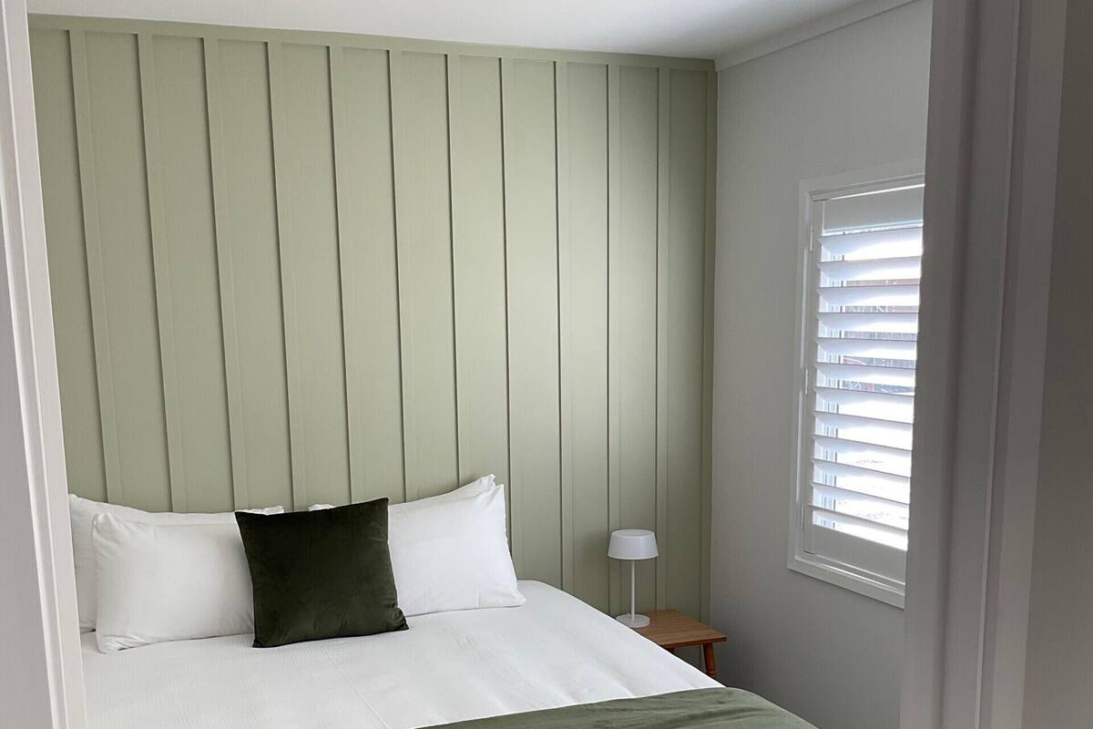 A bedroom with a bed, a nightstand, a lamp, and a window with blinds.