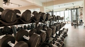 Een sportschool met rijen dumbbells op rekken, grote ramen en fitnessapparatuur op de achtergrond.