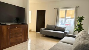 A modern living room with a flat-screen TV, a grey sofa, a wooden cabinet, and a potted plant. - Cancun - Next to the Sanctuary Maria untying of knots (Cancún)