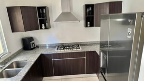 A modern kitchen with dark wood cabinets, a stainless steel refrigerator, a gas stove, and a built-in oven. - Cancun - Next to the Sanctuary Maria untying of knots (Cancún)