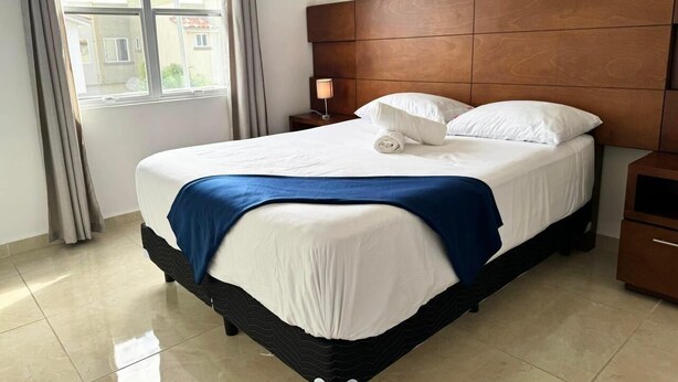 A neatly made bed with a blue blanket, a wooden headboard, and a nightstand with a lamp. - Cancun - Next to the Sanctuary Maria untying of knots (Cancún)