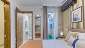 Een hotelkamer met een groot bed, een badkamer met een douchecabine van glas, uitzicht op een balkon en een schilderij aan de muur.
