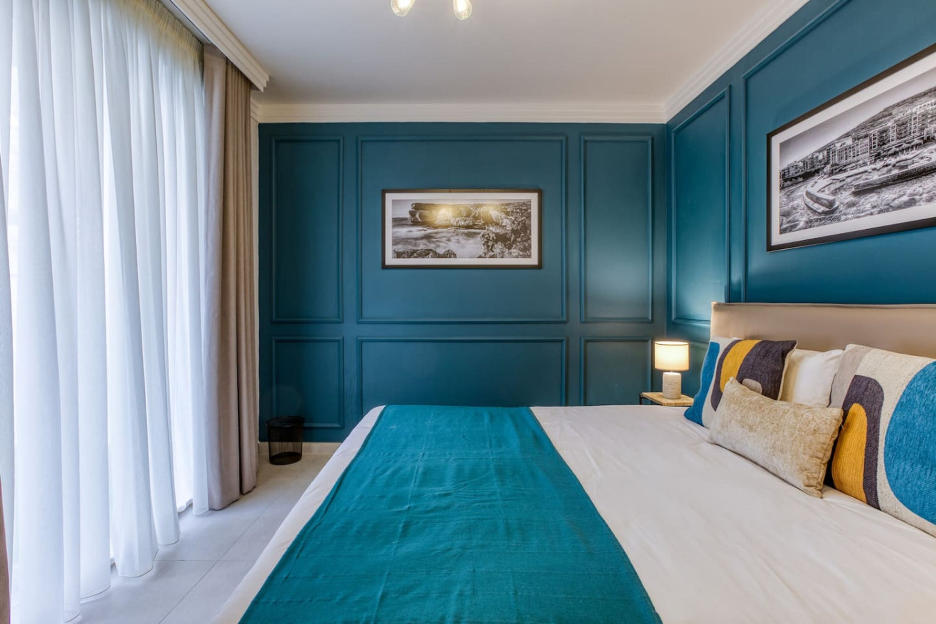A hotel room with a large bed, teal walls, and a framed picture on the wall.