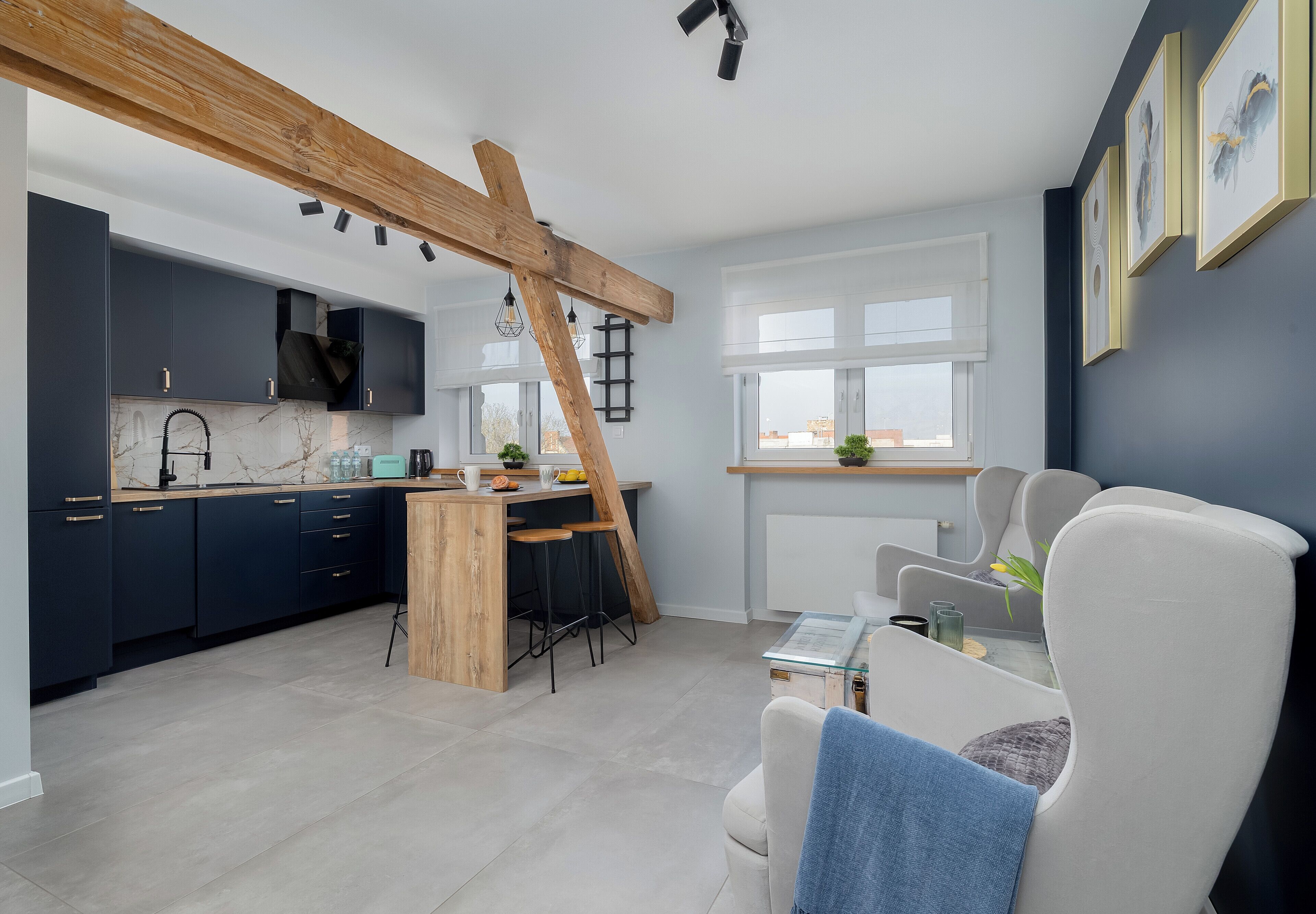 A modern kitchen with dark cabinets, a wooden beam ceiling, and a dining area with a white chair and table.