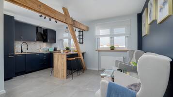 A modern kitchen with dark cabinets, a wooden beam ceiling, and a dining area with a white chair and table.
