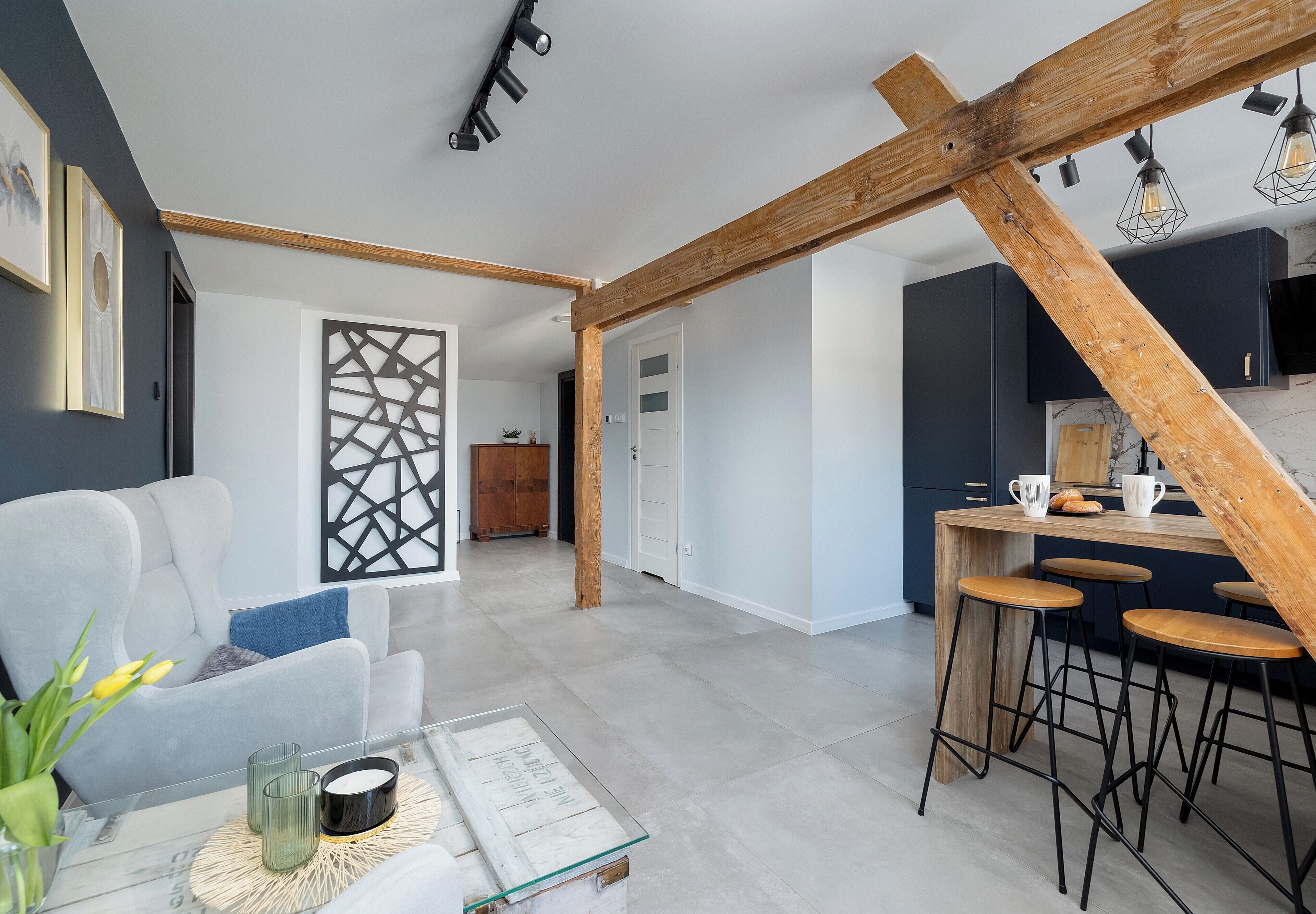 A modern living space with a kitchen area, wooden beams, and a dining set.