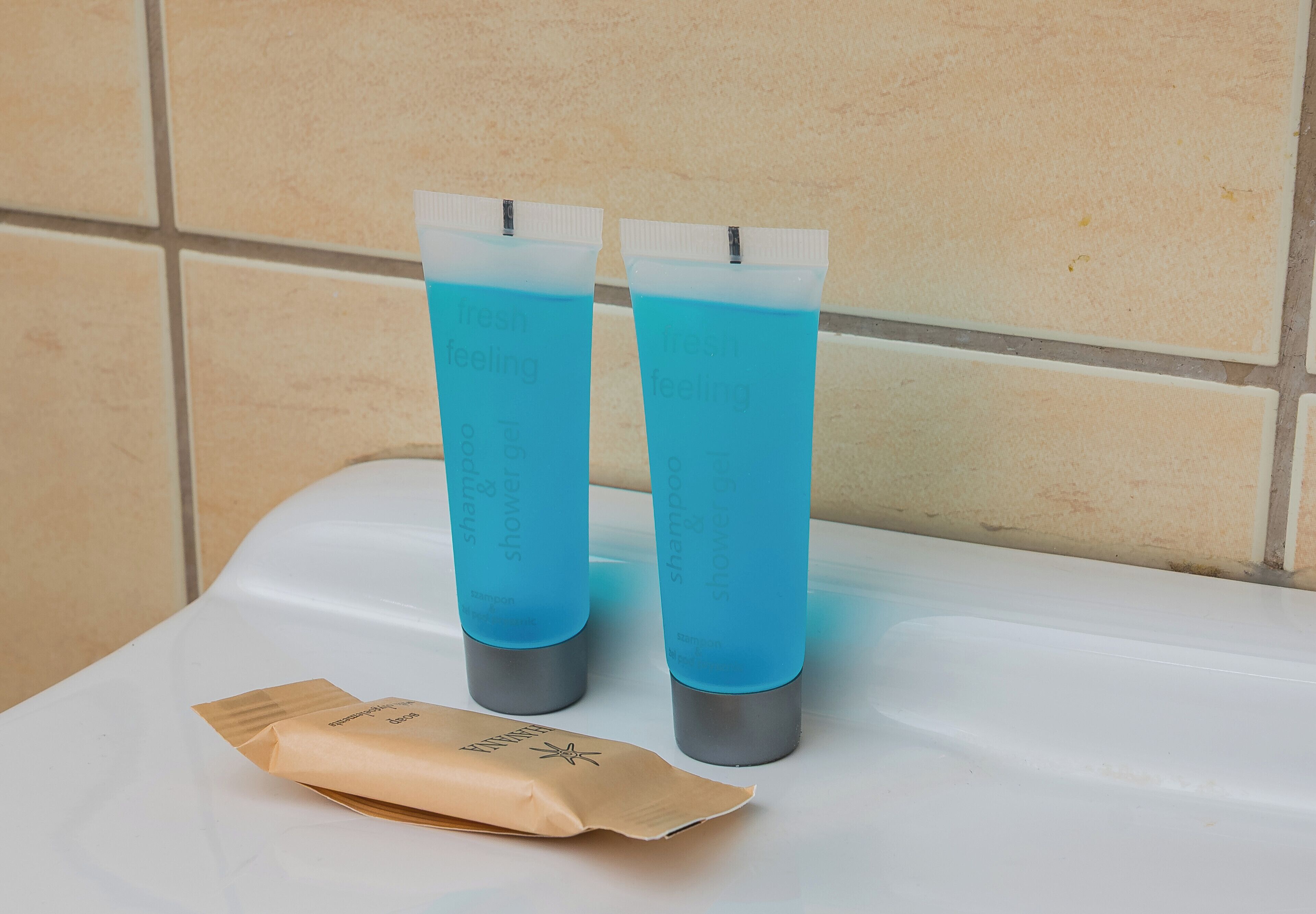 Dos botellas de líquido azul sobre una superficie blanca, con una pared de baldosas beige al fondo.