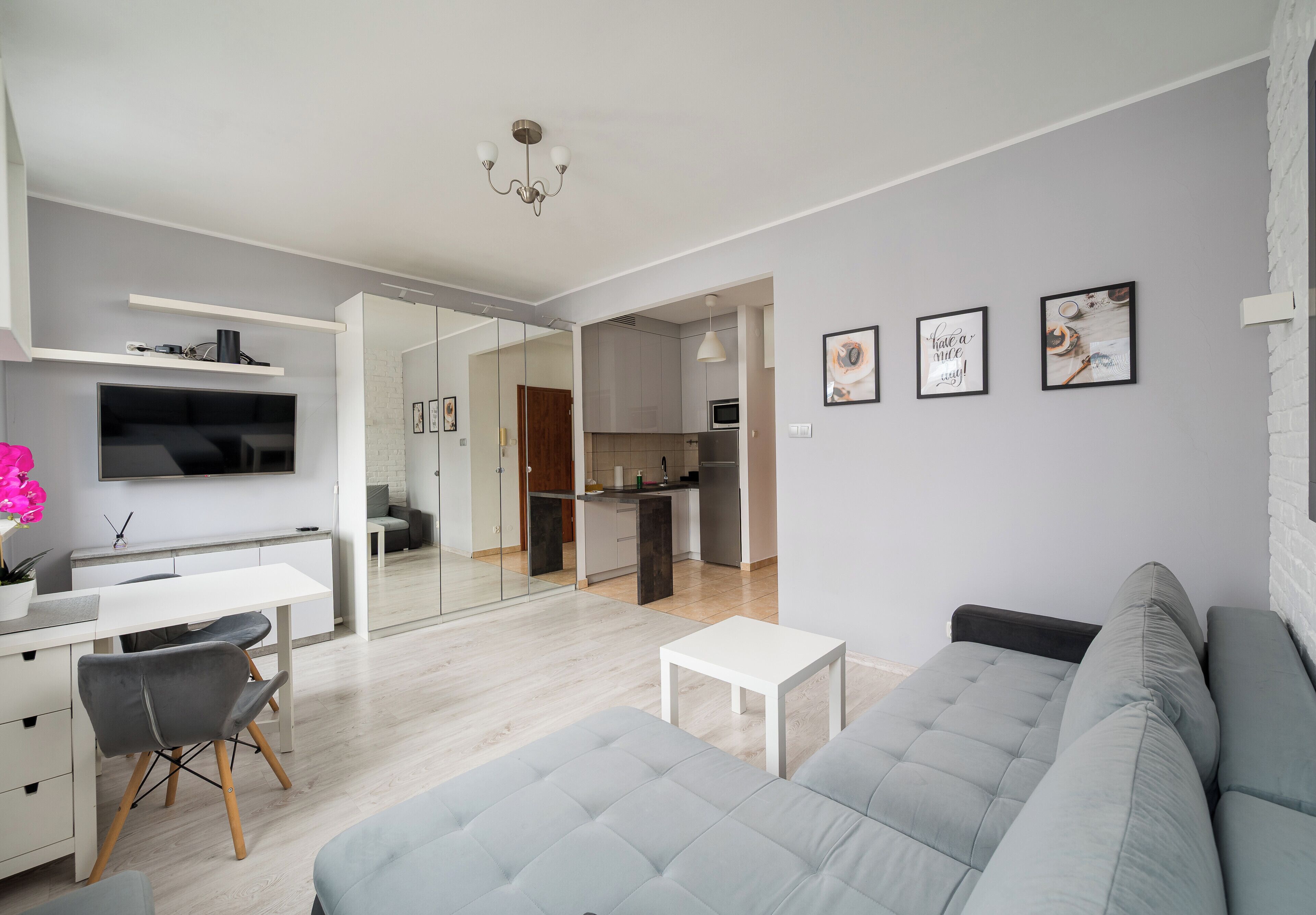 Una sala de estar moderna con un sofá gris, una mesa de centro blanca y un televisor montado en la pared.