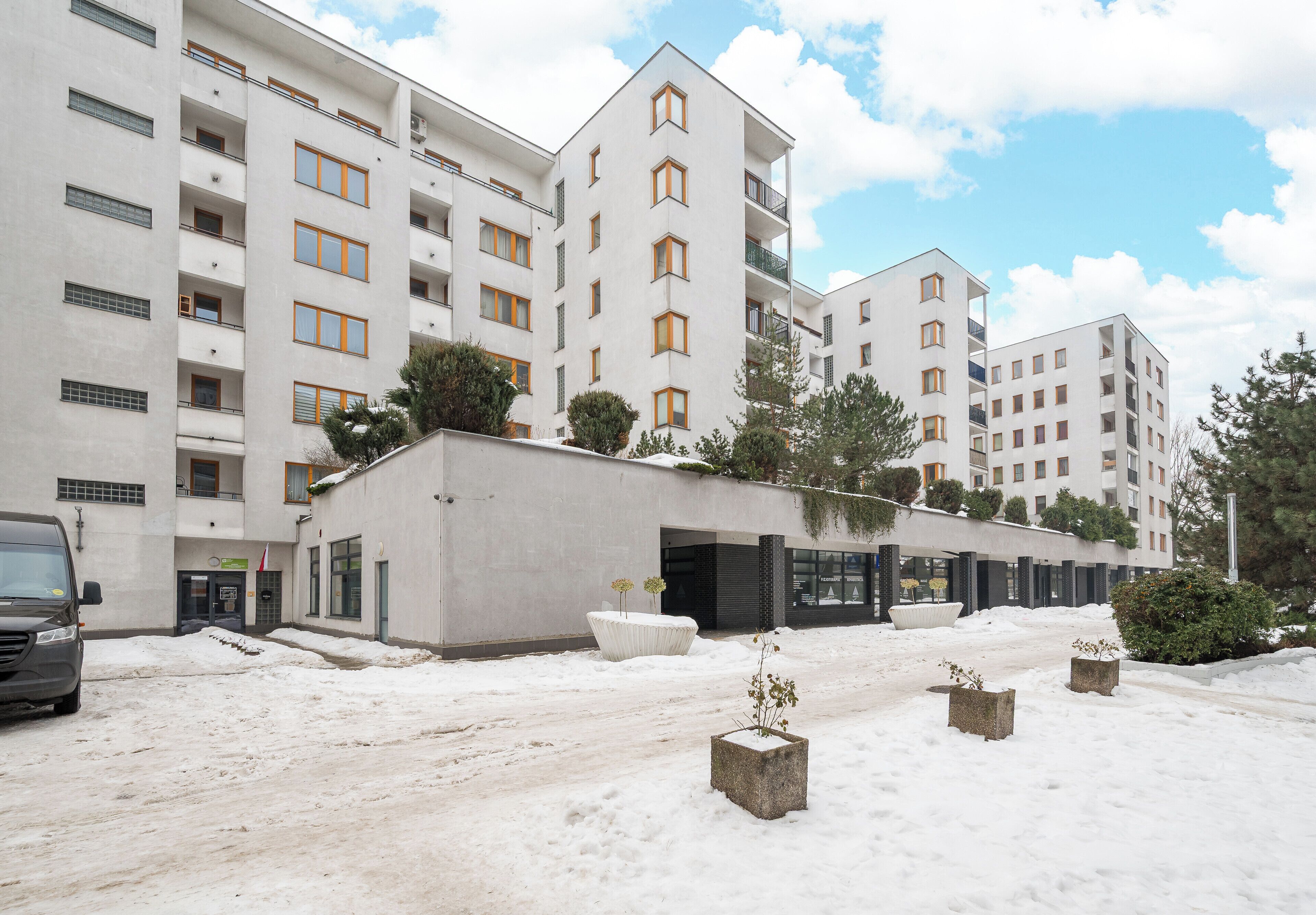 Un edificio residencial de varios pisos con balcones, un estacionamiento y suelo cubierto de nieve.
