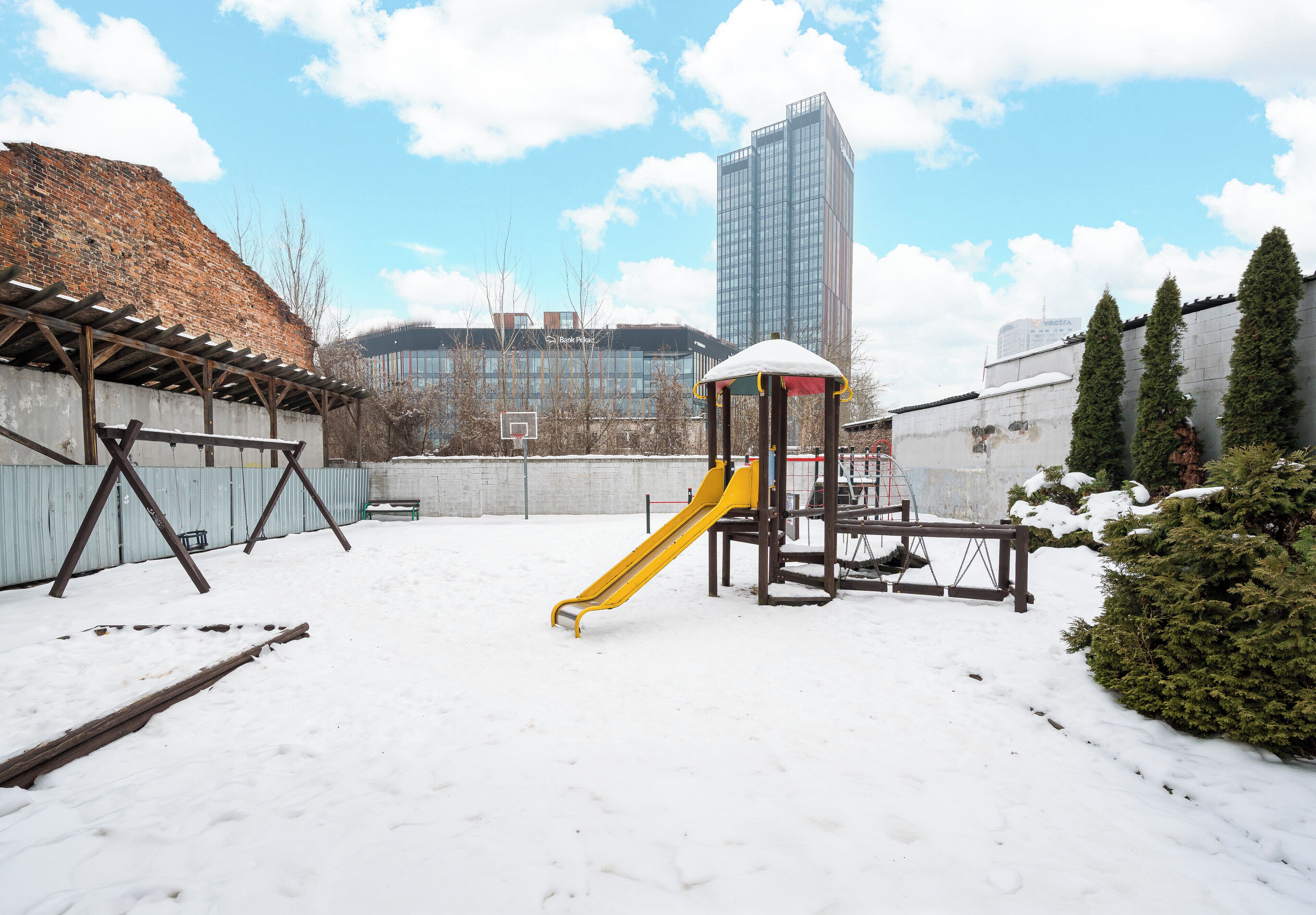 A playground with a yellow slide and a climbing structure, surrounded by snow.